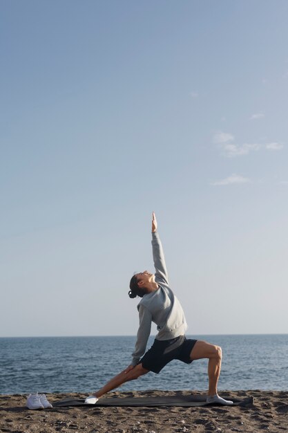 Hombre de tiro completo haciendo yoga en la playa