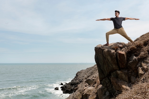 Hombre de tiro completo haciendo yoga en las rocas
