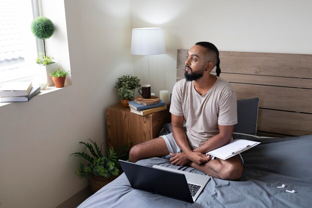 Hombre de tiro completo con laptop en la cama