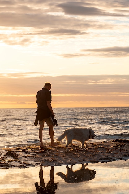 Hombre de tiro completo con lindo perro en la playa