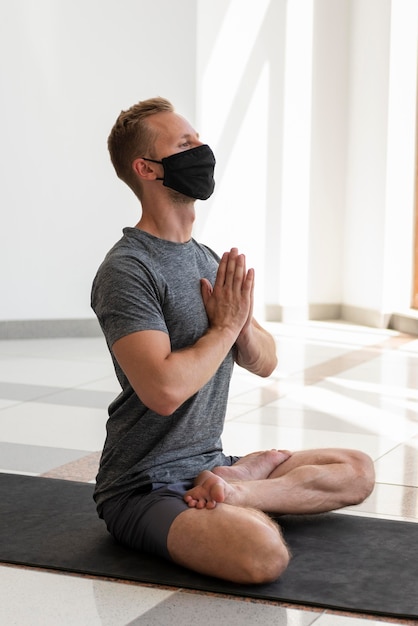 Hombre de tiro completo con mascarilla haciendo sukhasana en estera interior