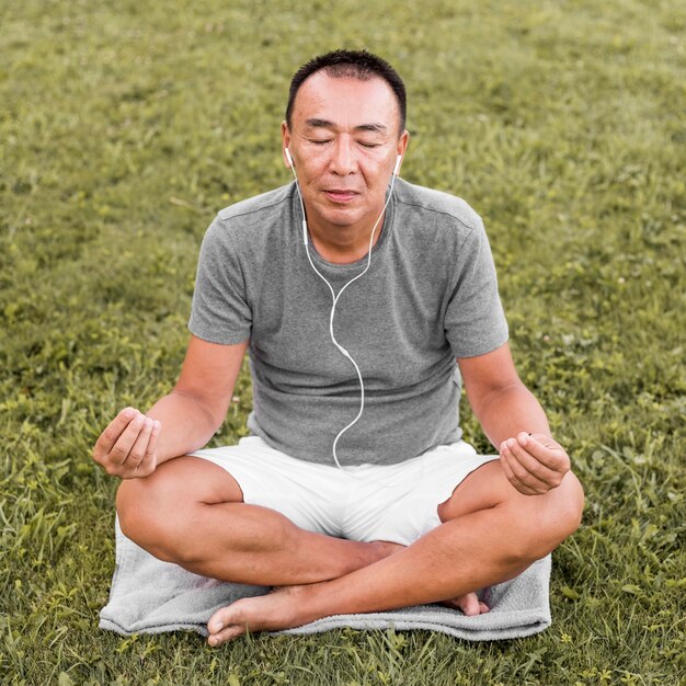 Hombre de tiro completo meditando sobre el césped