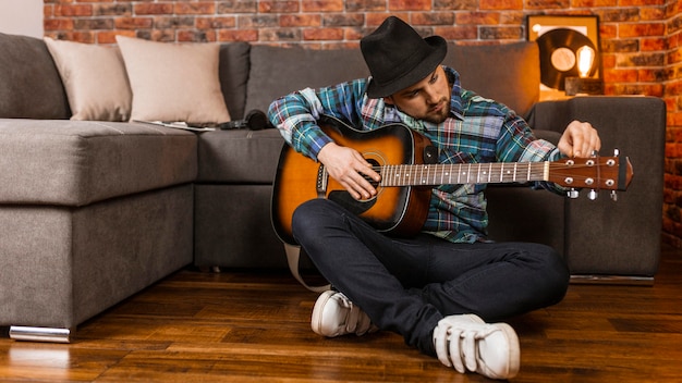 Hombre de tiro completo en el piso tocando la guitarra