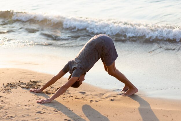 Hombre de tiro completo practicando yoga en la playa