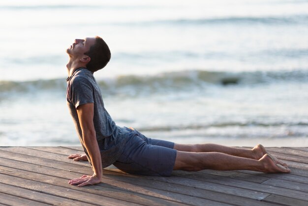 Hombre de tiro completo practicando yoga pose en el muelle cerca del mar