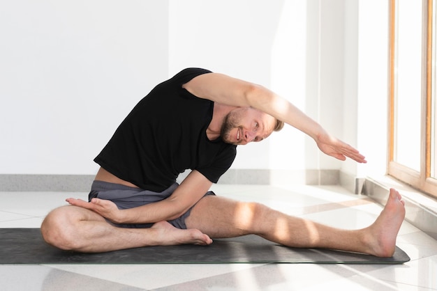 Hombre de tiro completo que se extiende sobre la estera de yoga interior