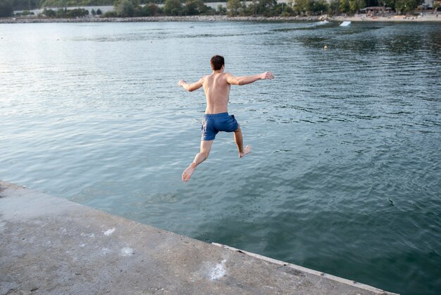 Hombre de tiro completo saltando en el agua vista posterior