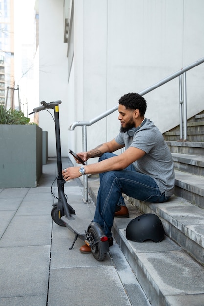 Hombre de tiro completo sentado en las escaleras con scooter eléctrico
