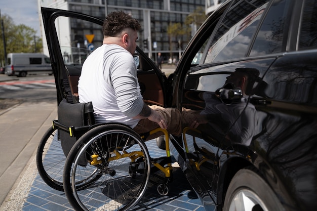 Hombre de tiro completo en silla de ruedas entrando al auto