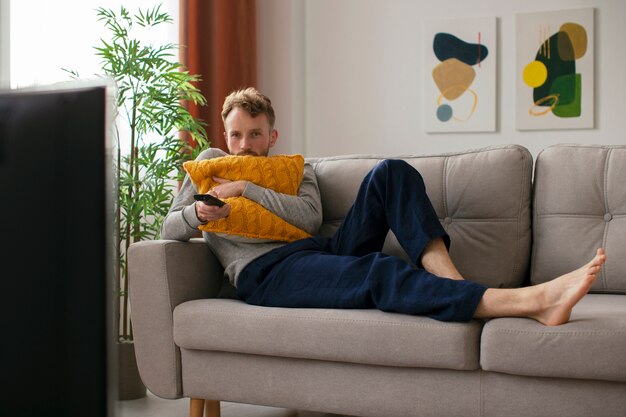 Hombre de tiro completo en el sofá viendo la televisión