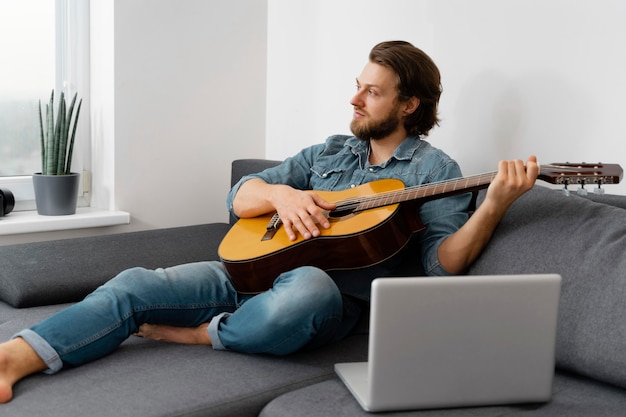 Hombre de tiro completo tocando la guitarra en casa