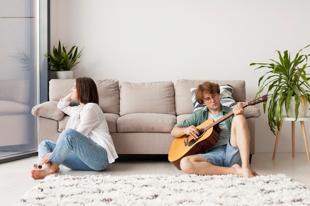 Hombre de tiro completo tocando la guitarra en interiores