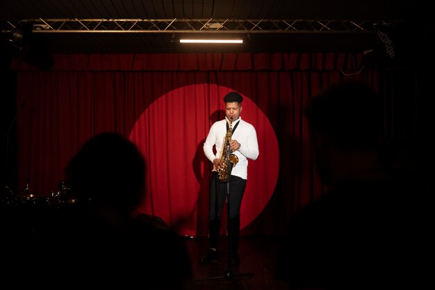 Hombre de tiro completo tocando el saxofón en el escenario