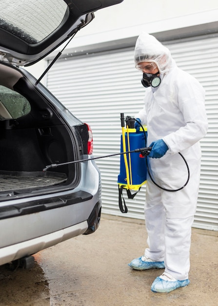 Hombre de tiro completo en traje de desinfectar el coche