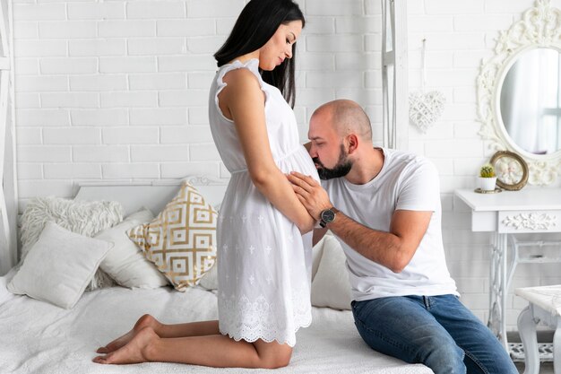 Hombre de tiro largo besando el vientre de su esposa