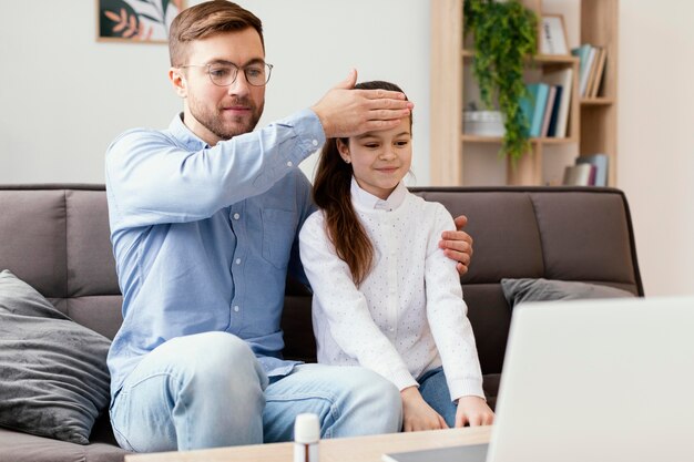 Hombre de tiro medio comprobando la temperatura de la niña