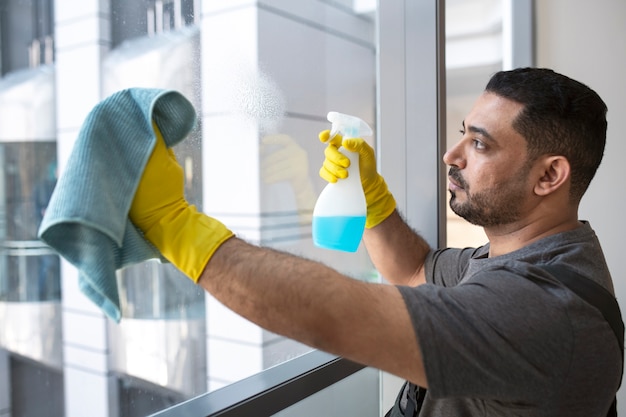 Hombre de tiro medio limpiando la ventana de la oficina