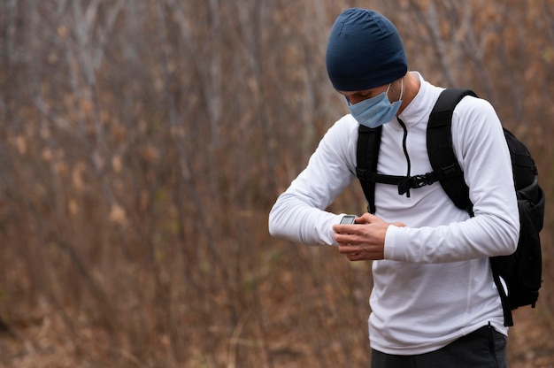 Hombre de tiro medio con mascarilla en el bosque mirando el reloj