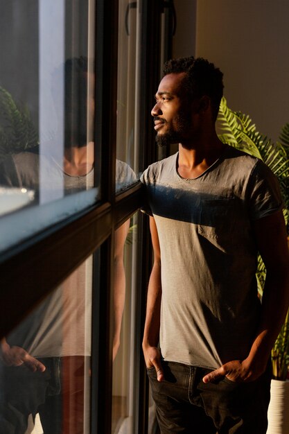 Hombre de tiro medio posando junto a la ventana