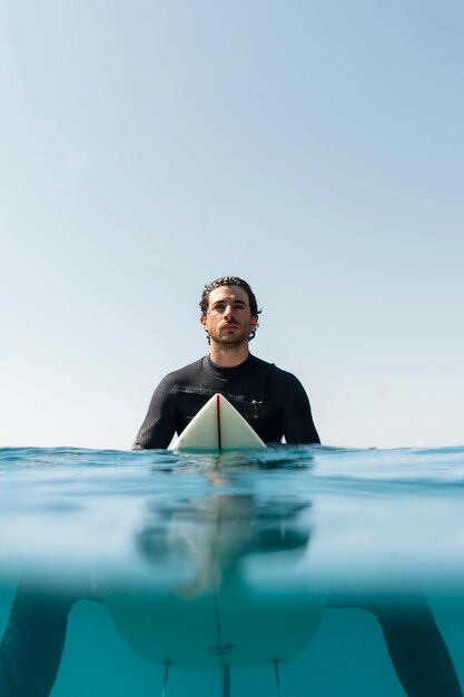 Hombre de tiro medio sentado en la tabla de surf