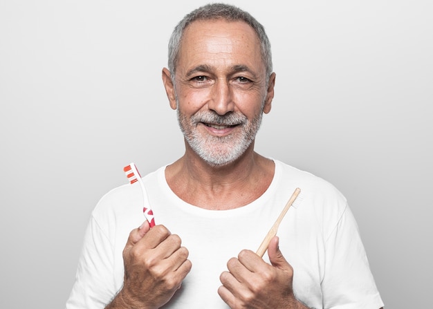 Hombre de tiro medio sosteniendo cepillos de dientes