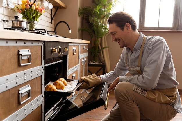 Hombre de tiro medio sujetando la bandeja con croissants