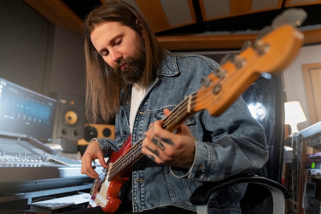 Foto gratuita hombre de tiro medio tocando la guitarra en el estudio