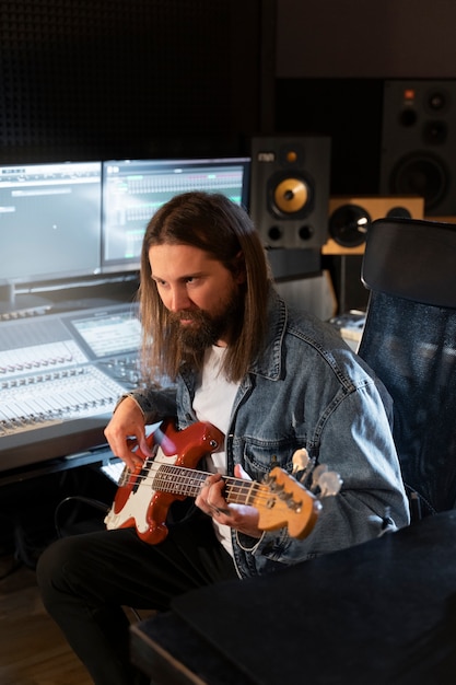 Foto gratuita hombre de tiro medio tocando la guitarra en el estudio