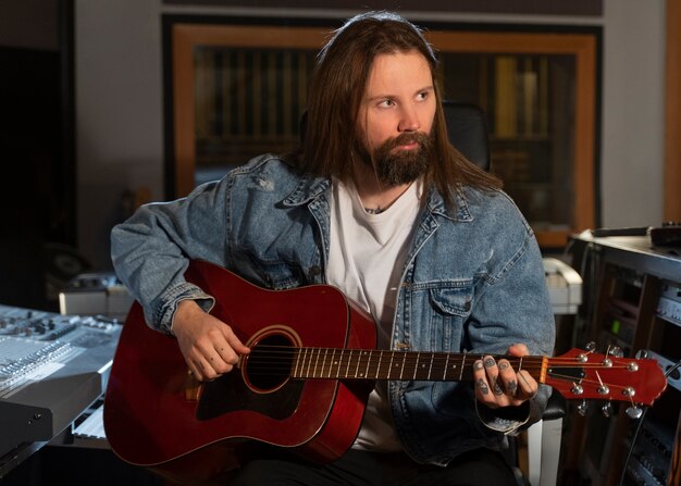 Hombre de tiro medio tocando la guitarra en el estudio