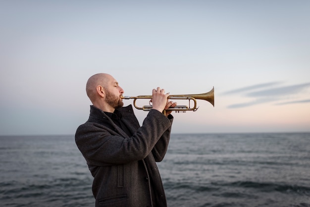 Foto gratuita hombre de tiro medio tocando la trompeta en la playa