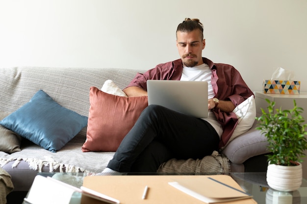 Hombre de tiro medio trabajando con un portátil en el sofá