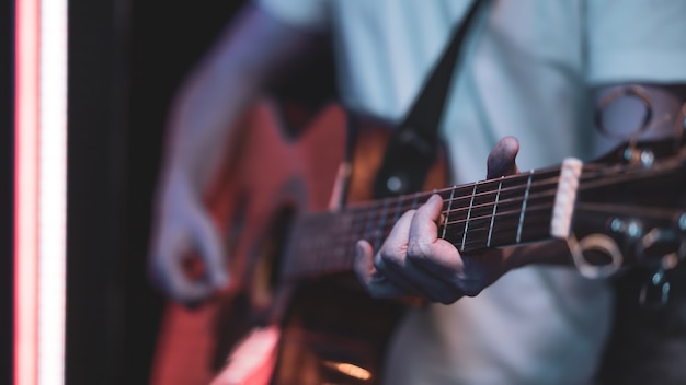 Un hombre toca una guitarra acústica en una habitación oscura. Actuación en vivo, concierto acústico.