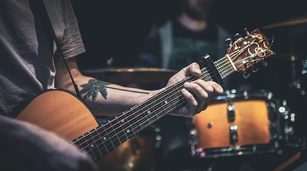 Un hombre toca una guitarra acústica en el primer plano oscuro