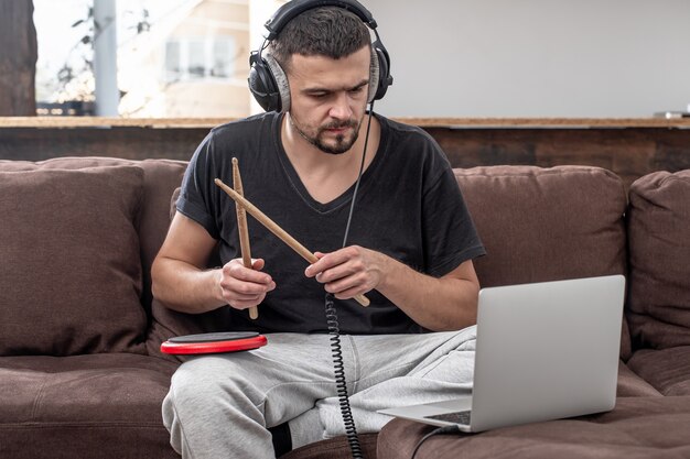 Un hombre toca el tambor y mira la pantalla del portátil. El concepto de lecciones de música en línea, lecciones de videoconferencia.