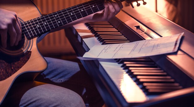 Hombre tocando la guitarra acústica y el piano de cerca, grabando notas, hermoso color de fondo, concepto de actividad musical