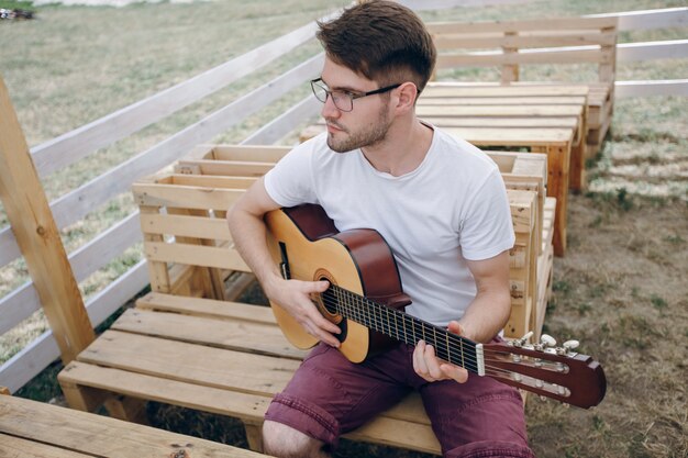 Hombre tocando la guitarra en unas mesas de madera con gafas de ver