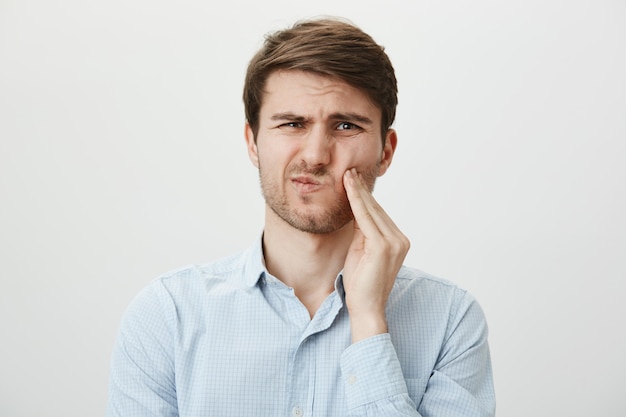 Foto gratuita hombre tocando la mejilla y haciendo muecas de dolor de muelas, necesita dentista