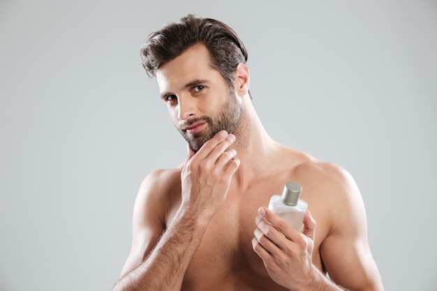 Hombre tocando su rostro mientras sostiene una botella de perfume