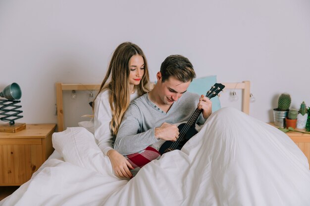 Hombre tocando el ukelele para mujer en la cama