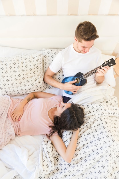 Hombre tocando el ukelele para mujer en la mañana