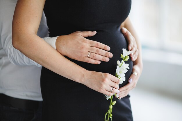 El hombre toma las manos para el vientre de su esposa embarazada, y la mujer sostiene una flor blanca