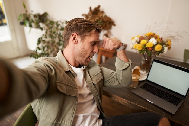 Foto gratuita hombre se toma una selfie en el teléfono móvil flexionando los bíceps muestra sus músculos a la cámara hace fotos en un café