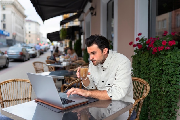 Hombre tomando un café helado mientras usa una computadora portátil