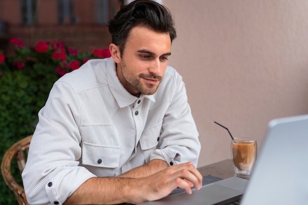 Hombre tomando un café helado mientras usa una computadora portátil