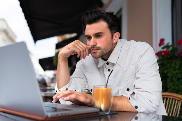 Hombre tomando un café helado mientras usa una computadora portátil