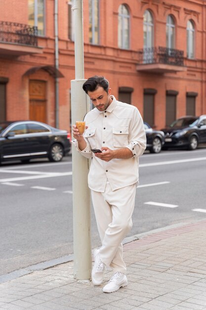 Hombre tomando un café helado mientras usa un teléfono inteligente al aire libre