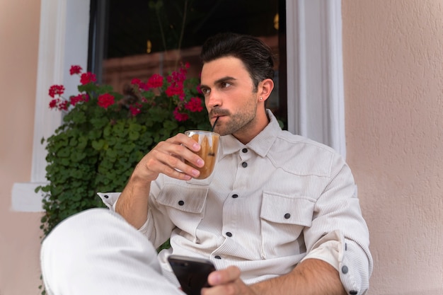 Hombre tomando un café helado mientras usa un teléfono inteligente