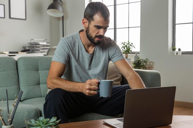 Hombre tomando café y trabajando desde casa en la computadora portátil