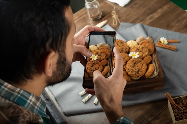 Hombre tomando foto de bandeja de galletas con su teléfono inteligente