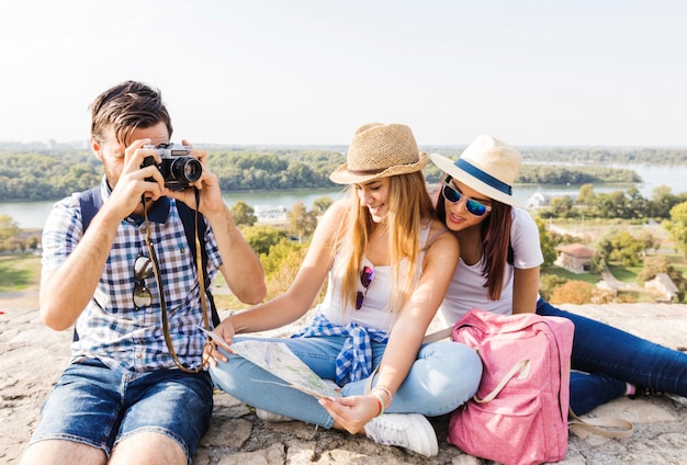 Foto gratuita hombre tomando fotos en la cámara cerca de sus amigas mirando el mapa